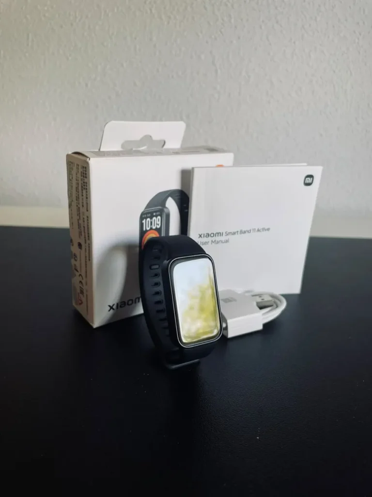 Xiaomi Smart Band 11 Active negra delante de su caja, con el manual de usuario y el cable de carga.