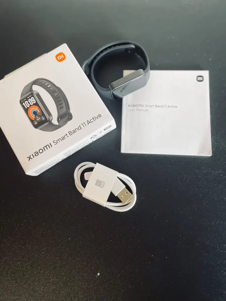 Contenido de la caja de la Xiaomi Smart Band 11 Active: pulsera negra, manual de usuario y cable de carga USB.
