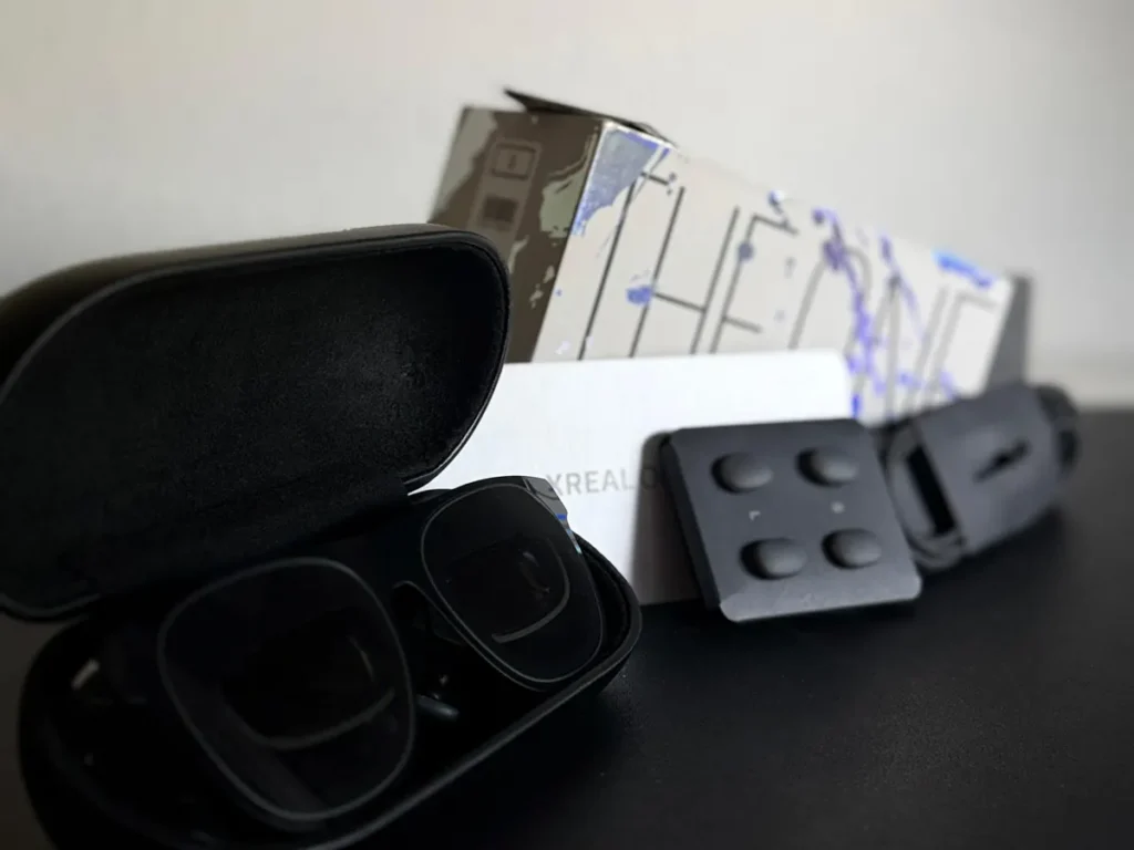 Estuche abierto con las gafas XREAL One dentro, almohadillas nasales y cable USB-C delante de la caja.